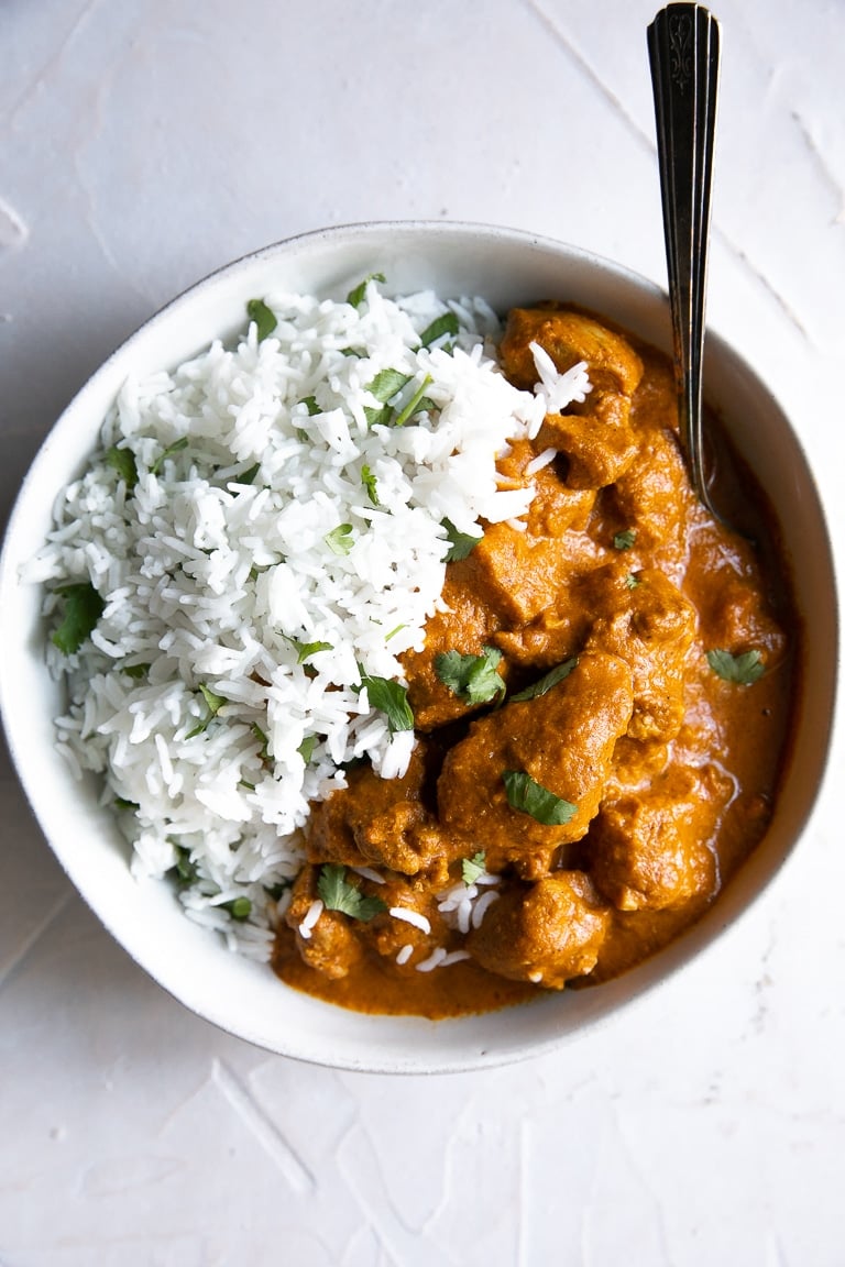 White serving bowl filled with cooked chicken tikka masala curry in a sauce seasoned with garam masala, cream, and butter.