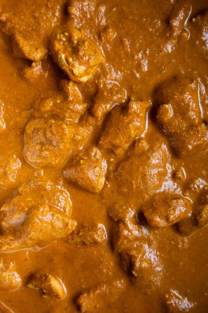 Close up image of a pot filled with chicken thigh pieces stewing in a rich and creamy curry sauce.