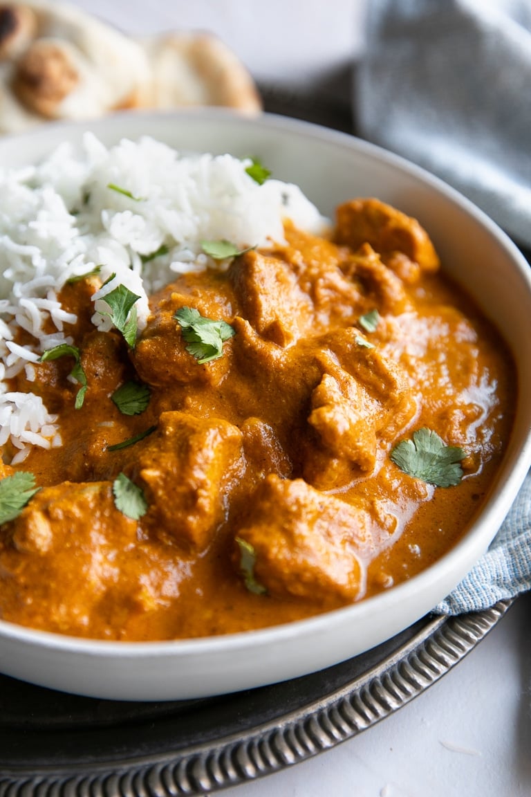 White serving bowl filled with chicken tikka masala and basmati rice garnished with fresh cilantro.