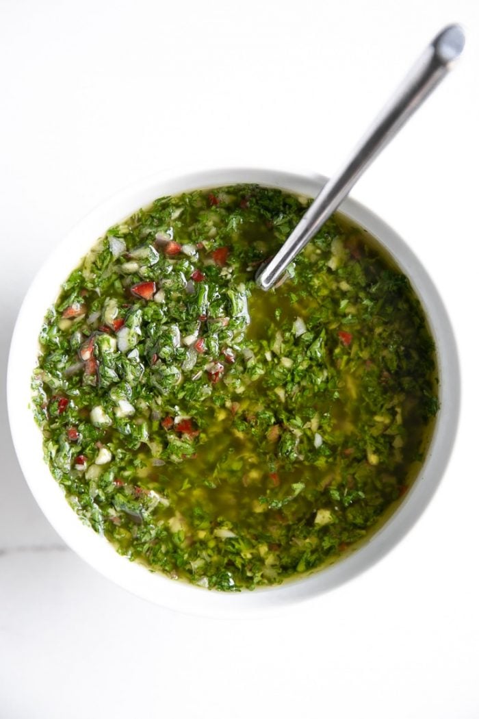 White bowl with a spoon filled with green Chimichurri.