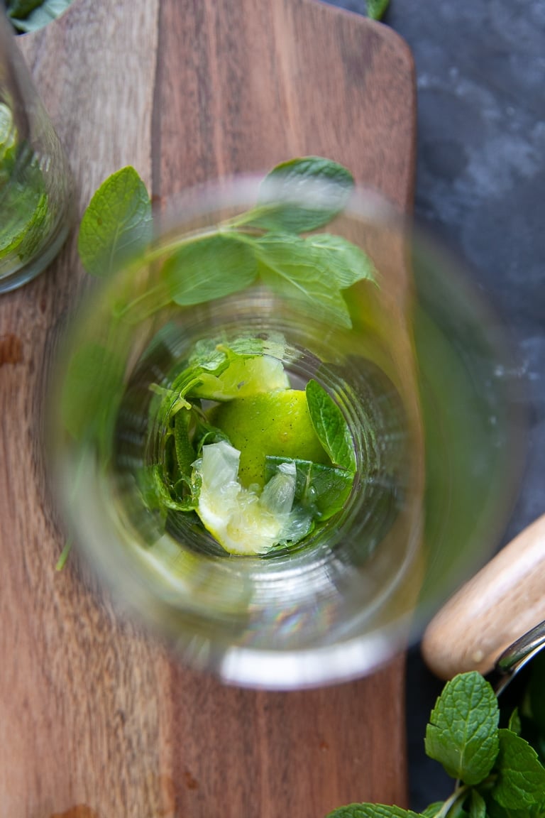 Overhead image of a highball glass filled with muddled lime and fresh mint.