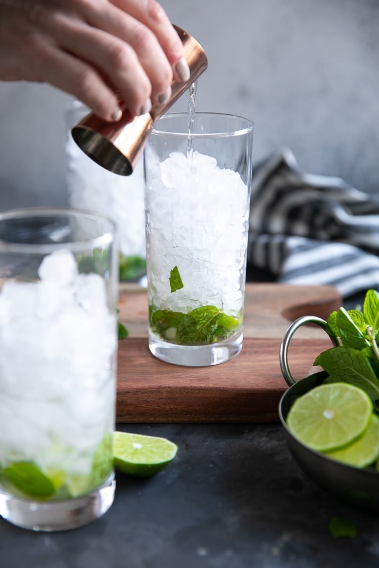 White rum being poured into a highball glass filled with muddled lime, mint and filled with crushed ice.