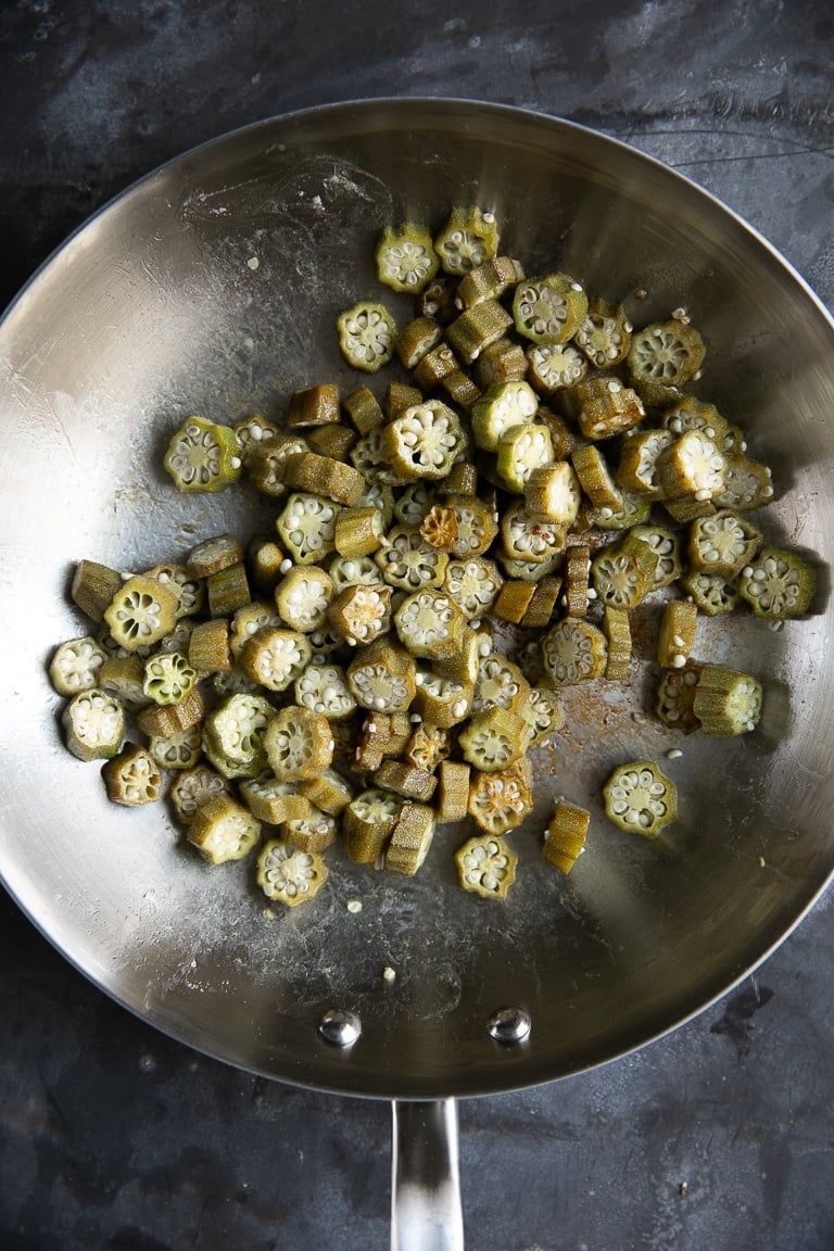 Image of chopped okra in a large stainless steel skillet cooking.