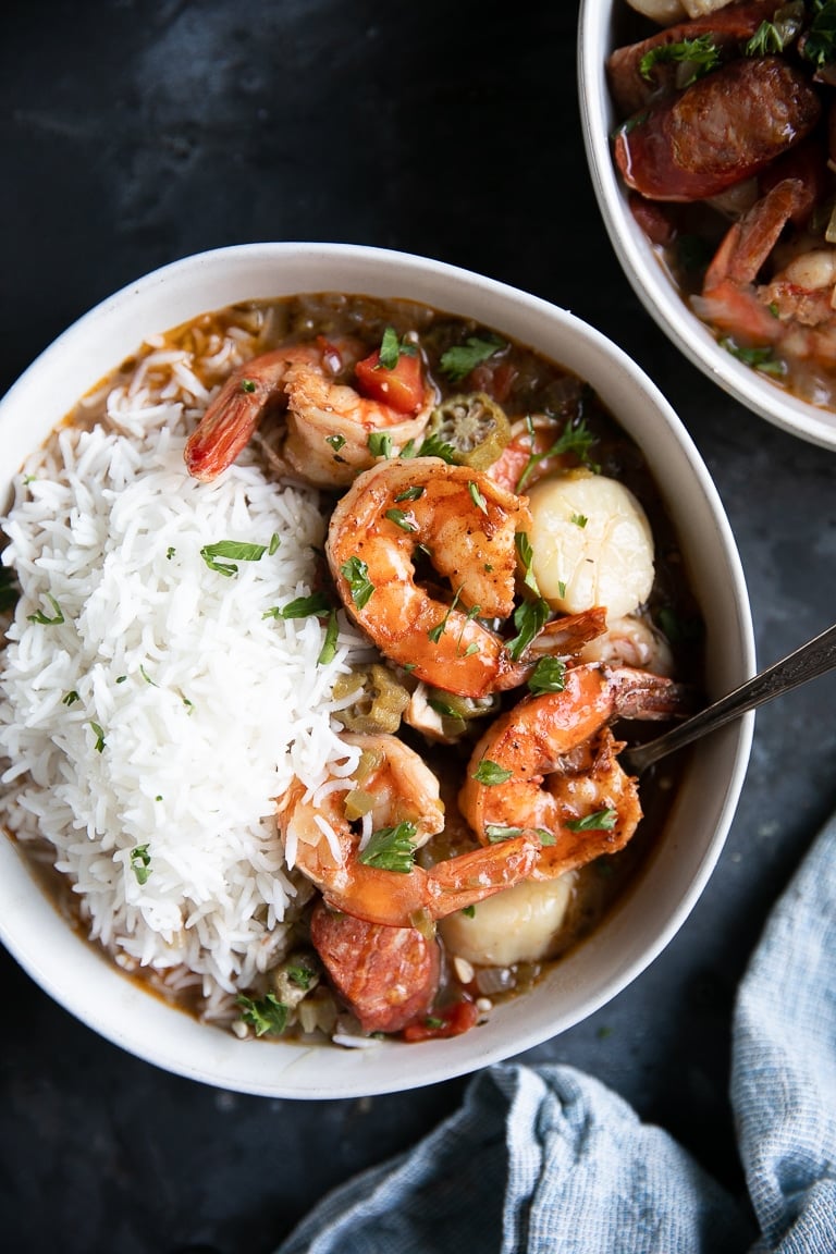 Large white bowl filled with seafood and sausage gumbo with white rice.