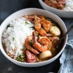 Shrimp, chicken, and sausage gumbo in white bowls and served with white rice.