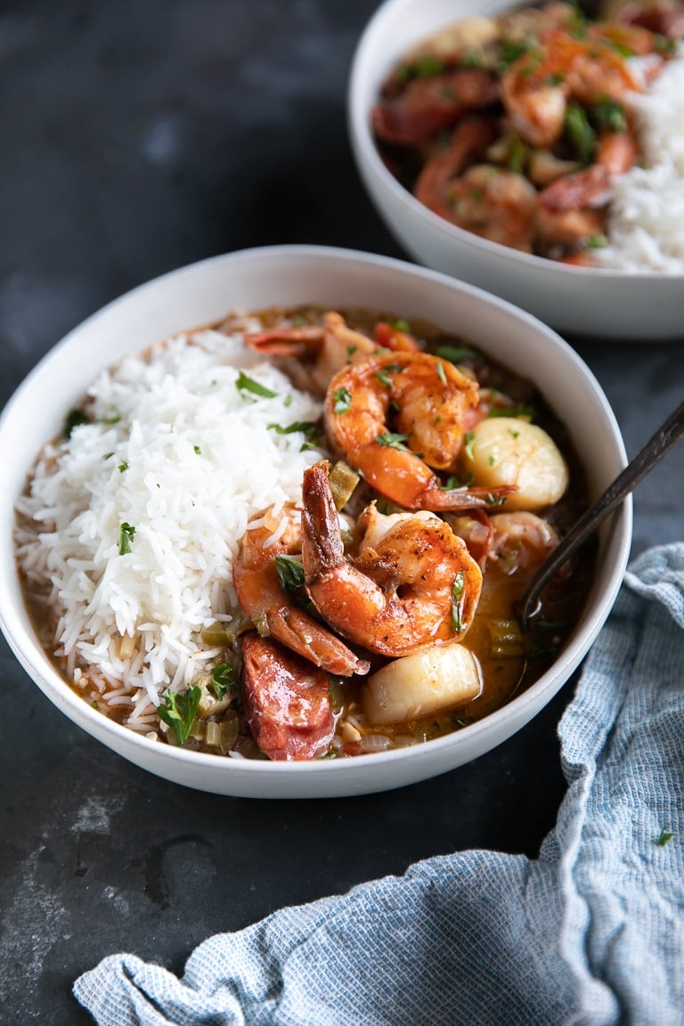 Shrimp, chicken, and sausage gumbo in white bowls and served with white rice.