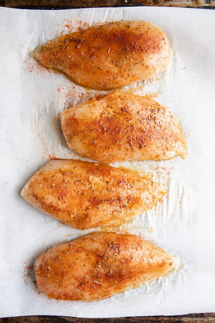 Four large boneless skinless chicken breasts coated in olive oil, salt, black pepper, paprika, and Cajun seasoning, and placed on a large baking sheet in a single layer.