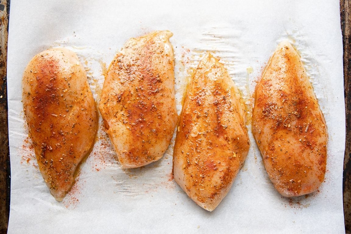 Four large boneless skinless chicken breasts coated in olive oil, salt, black pepper, paprika, and Cajun seasoning, and placed on a large baking sheet in a single layer.