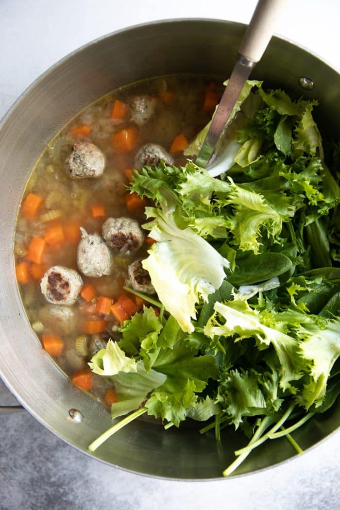 Fresh greens being added to pot of cooking Italian Wedding Soup