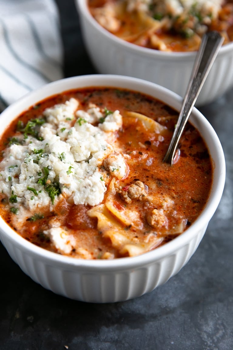 White bowl filled with lasagna soup and topped with ricotta cheese.