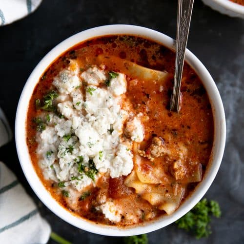 White bowl filled with lasagna soup and topped with ricotta cheese.