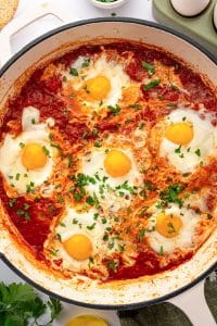 Close-up of shakshuka with poached eggs in tomato sauce and chopped parsley.