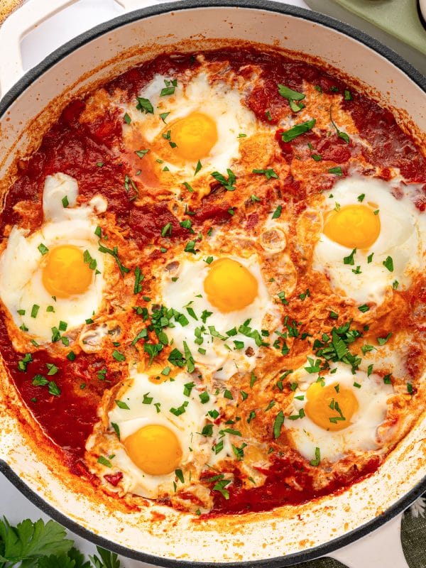 Close-up of shakshuka with poached eggs in tomato sauce and chopped parsley.
