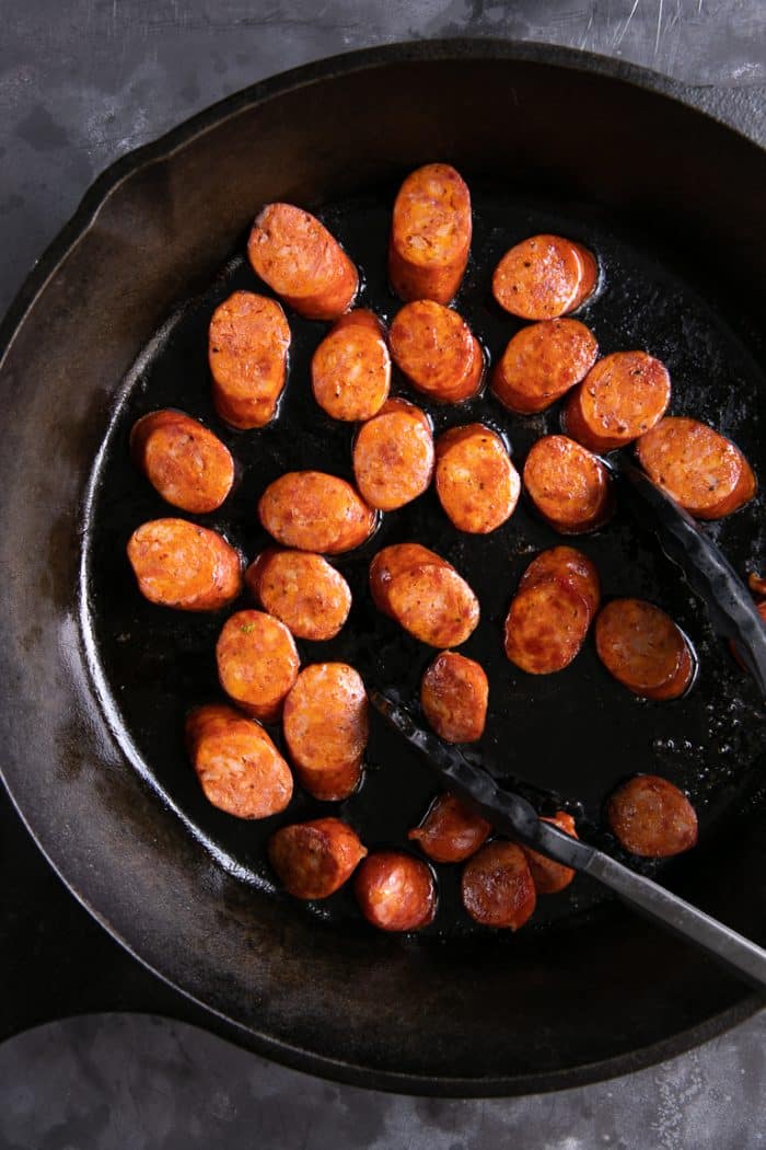 Andouille sausage cooking in a cast iron skillet.