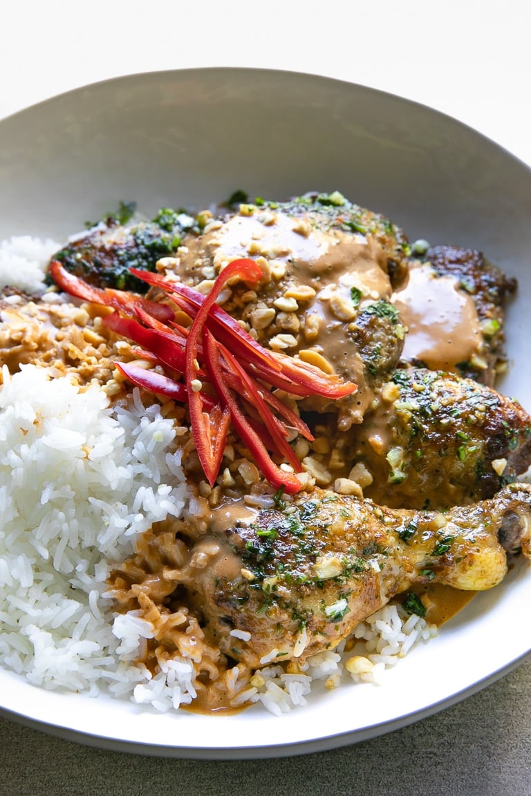 Large serving bowl filled with rice, grilled Thai chicken, Thai peanut sauce, and garnished with crushed peanuts and sliced red chilis.
