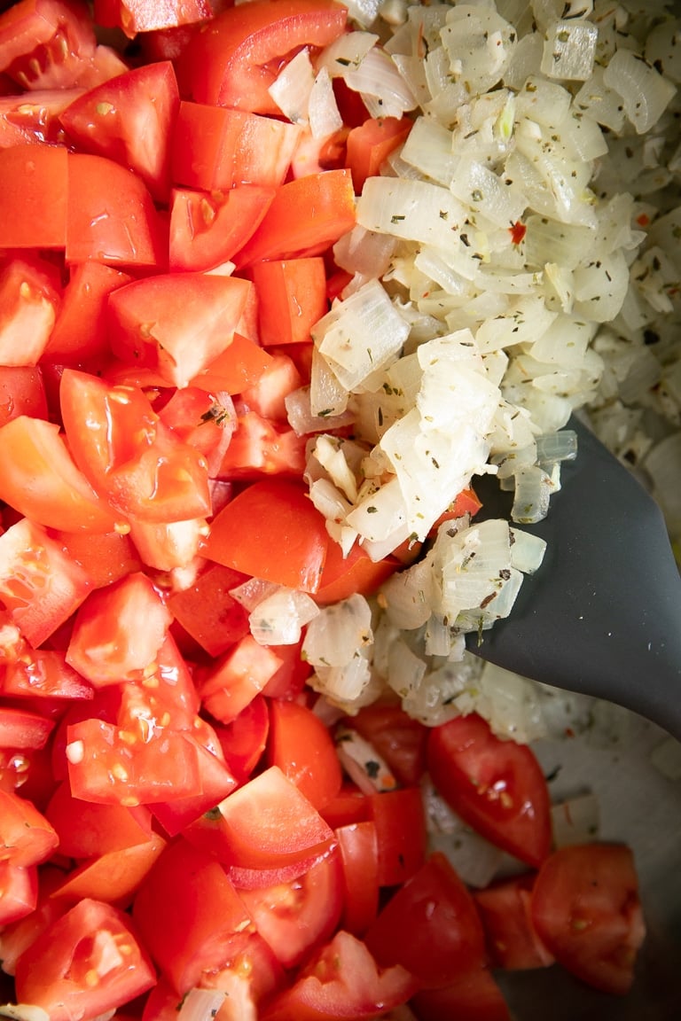 Close-up image of the sauteed onions mixed in Italian seasoning with fresh tomatoes.