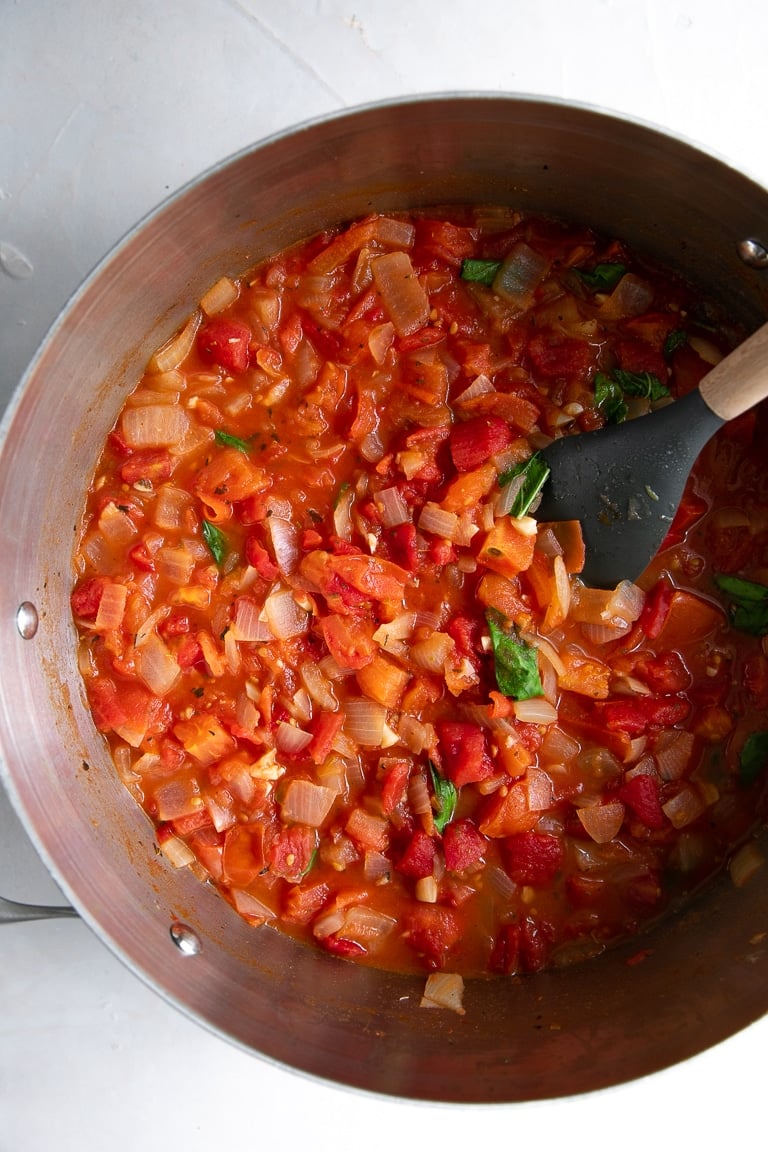 Large pot filled with sauteed tomatoes, onions, garlic, and fresh basil.