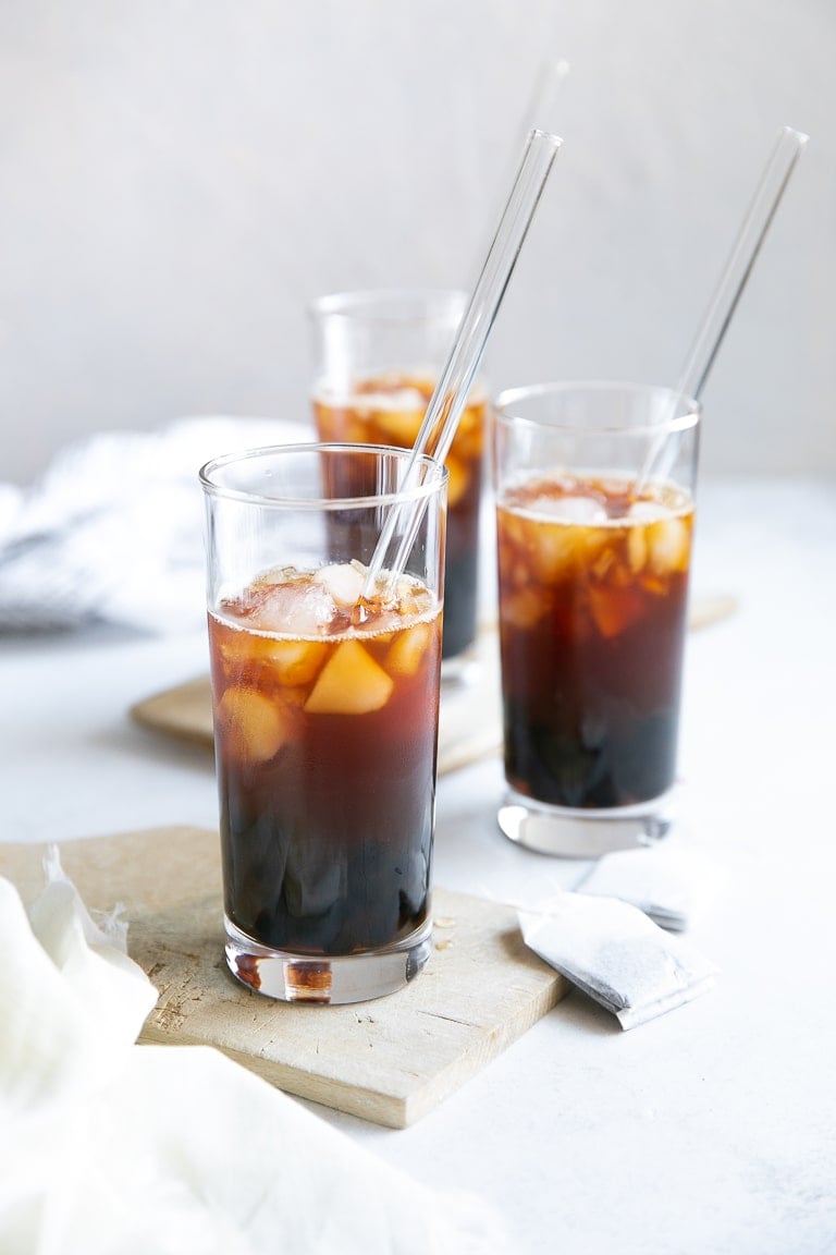 Three clear glasses filled with black tea, boba, and ice.