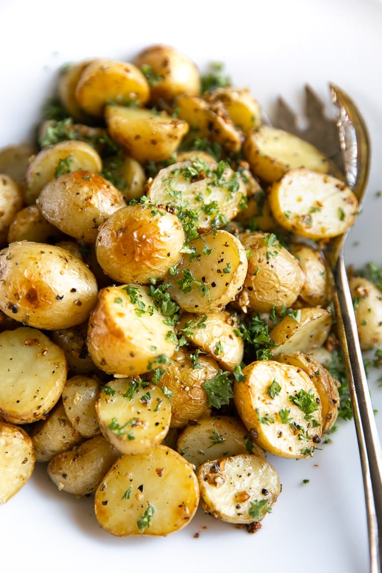 Large white bowl filled with Garlic Roasted Potatoes and sprinkled with fresh chopped parsley.