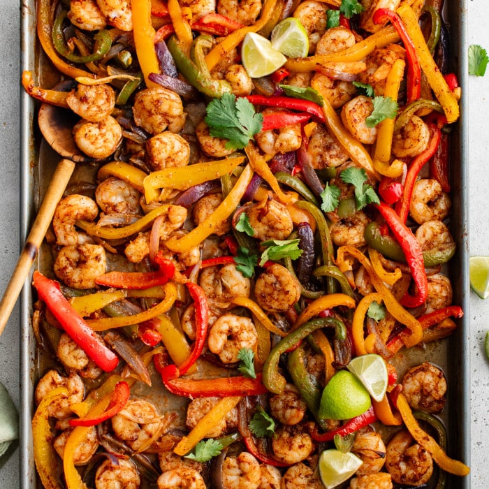 Square cropped overhead of colorful shrimp fajitas with lime wedges and cilantro.