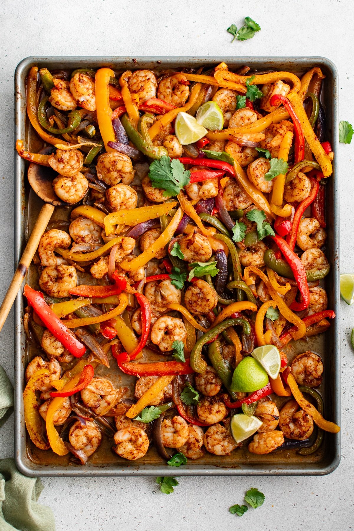 Overhead view of shrimp fajitas on a sheet pan with bell peppers, onions, lime wedges, and fresh cilantro.