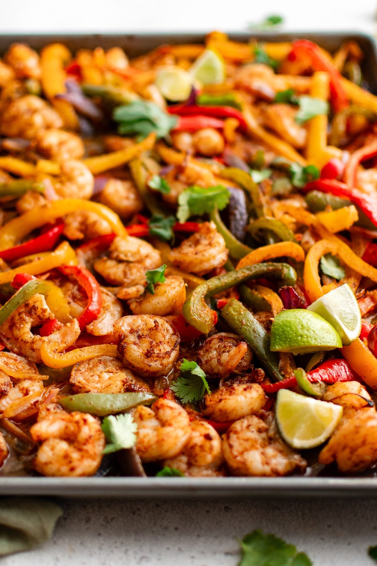 Close-up of roasted shrimp fajitas on a sheet pan with bell peppers, red onions, cilantro, and lime wedges.
