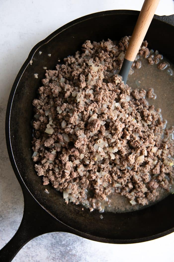 Ground beef and onions cooking in a large black cast iron skillet.