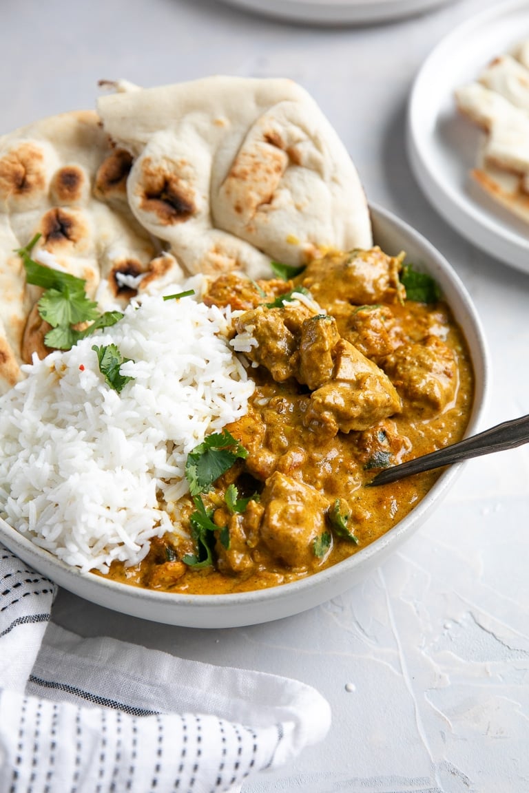 White bowl filled with creamy butter chicken and rice served with naan bread.