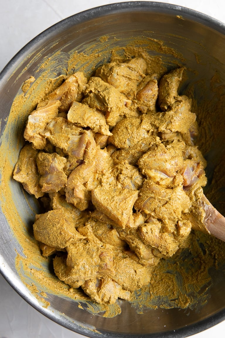 butter chicken marinade fully coating chicken in a mixing bowl