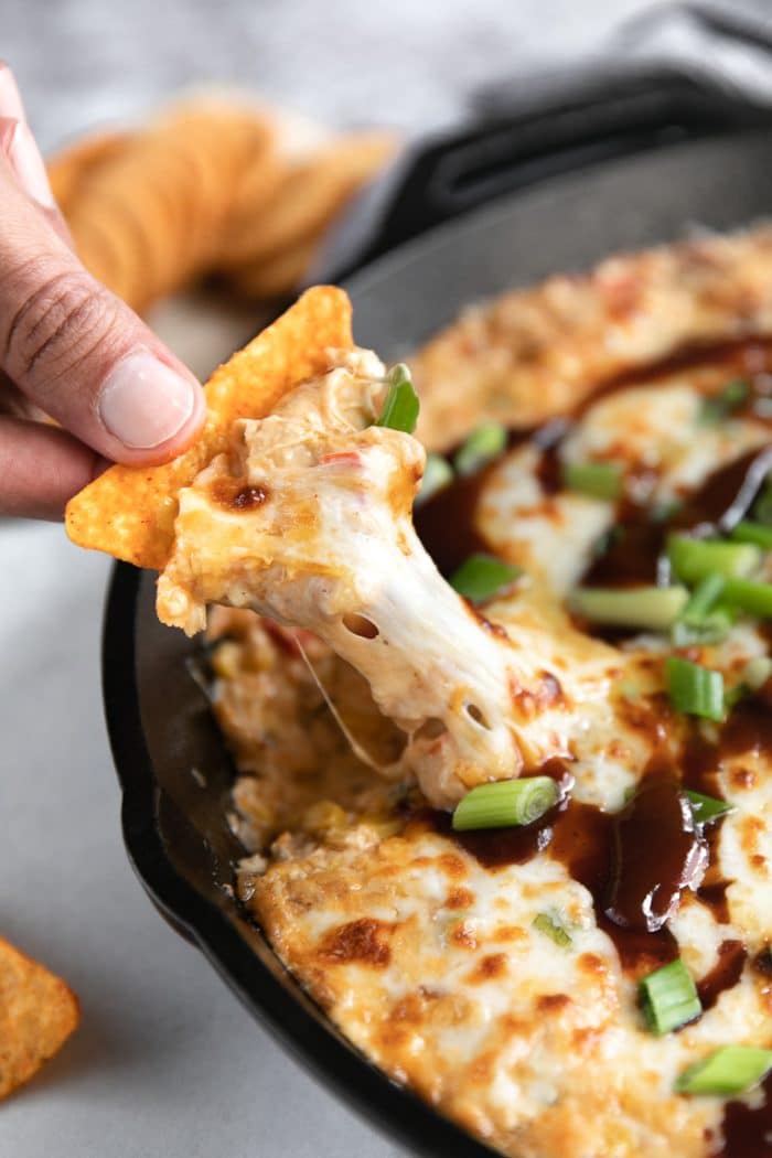 Doritos chip scooping out a hot and cheesy bbq chicken dip from a black cast iron skillet.