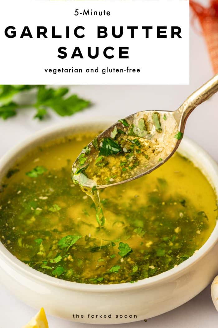 Vertical Pinterest pin with a large white text box at the top that reads “5-Minute GARLIC BUTTER SAUCE” in bold black letters and “vegetarian and gluten-free” in smaller black text underneath. Below the text box is a close-up photo of a white ceramic bowl filled with golden garlic butter sauce flecked with chopped parsley. A gold spoon is lifted above the bowl with sauce dripping back in. Lemon wedges and whole garlic bulbs sit near the bottom edge, a soft-focus parsley bunch is in the background, and an orange fringed napkin is visible at the right. Small black text at the bottom reads “the forked spoon.”
