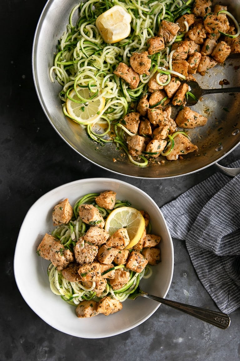 Skillet and white bowl filled with zucchini noodles and garlic butter chicken bites.