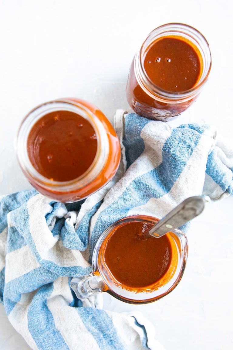 Overhead image of homemade red enchilada sauce in three glass jars.