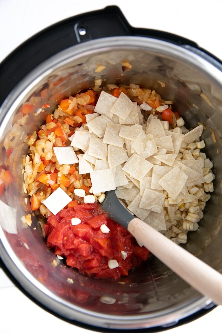Instant pot filled with sauteing onions, bell pepper, corn, and tomatoes.