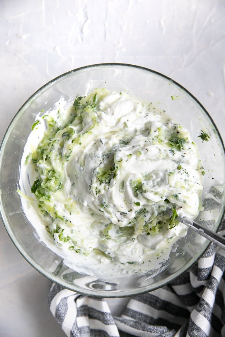 All the ingredients to make homemade tzatziki mixed together in a medium sized glass bowl.