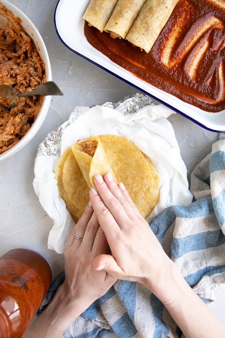 Rolling a corn tortilla filled with shredded chicken.
