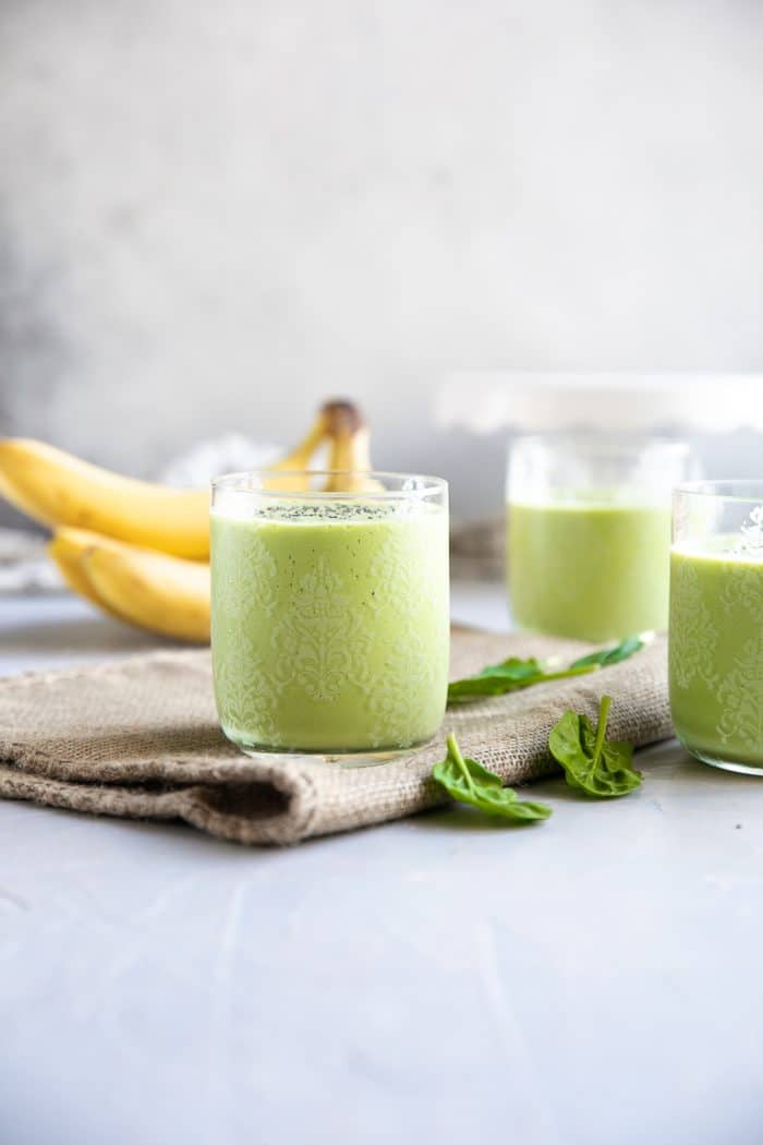 Three glasses filled with green smoothie made with yogurt, milk, spinach, mango, peach, and chia seeds.