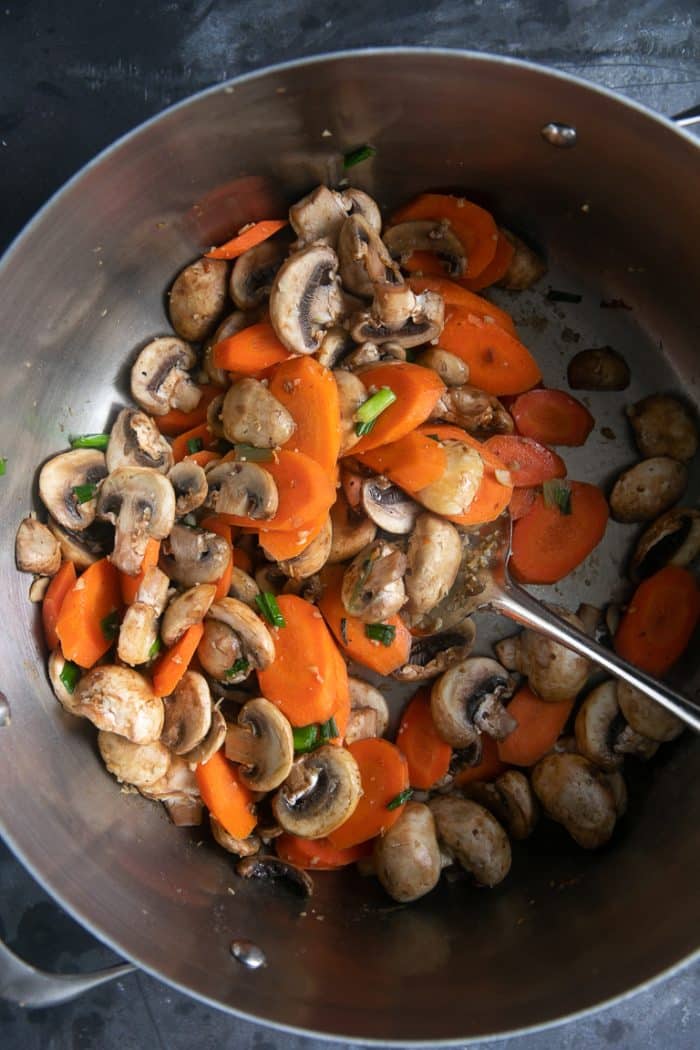 Mushrooms and carrots cooking in a large pan.