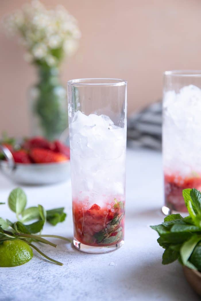 Muddled mint, lime, strawberries, and simple syrup in a tall glass topped with ice.