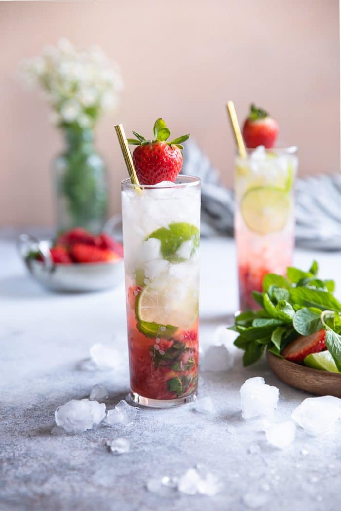 Two highball glasses filled with strawberry mojitos and garnished with a strawberry and gold straw.
