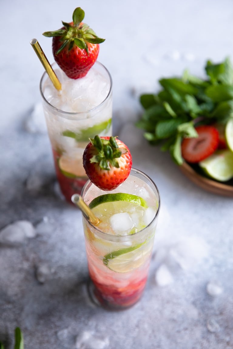 Overhead image of two strawberry mojitos with gold straws and strawberry garnish.