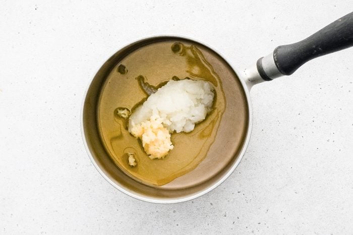 A medium saucepan set over medium heat filled with shredded onion and minced garlic.