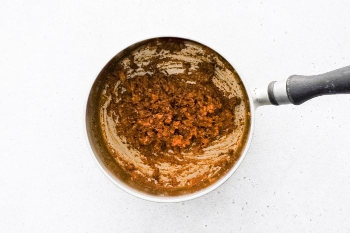 A paste of softened onion, garlic, olive oil, paprika, garlic powder, mustard, and chili powder cooking in a medium saucepan.
