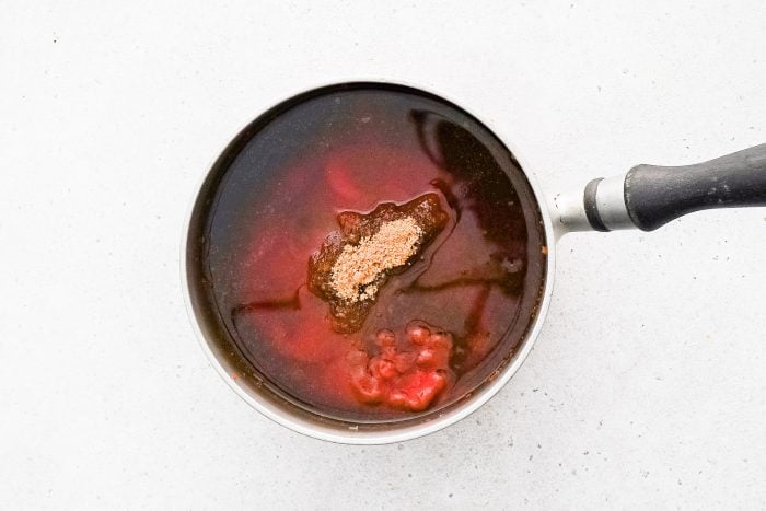 Ketchup, apple juice, brown sugar, apple cider vinegar, Worcestershire sauce, and honey added to a medium saucepan set over medium heat filled with a paste consisting of softened onion, garlic, olive oil, paprika, garlic powder, mustard, and chili powder.