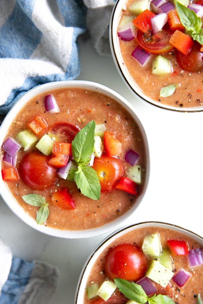 Bowls of gazpacho topped with diced cucumber, tomato, red onion, and bell pepper.