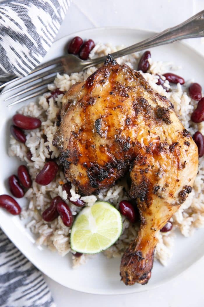 Overhead image of grilled jerk chicken on a white plate with Jamaican rice and peas.
