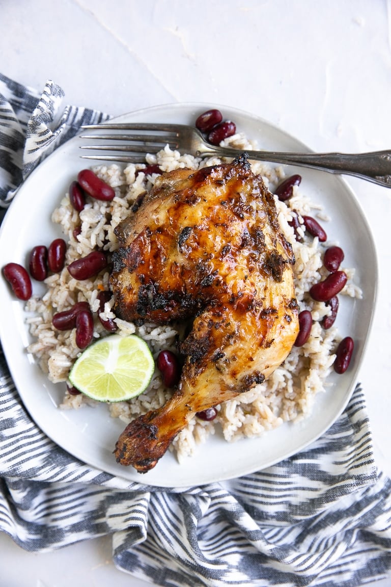Overhead image of grilled jerk chicken on a white plate with Jamaican rice and peas.