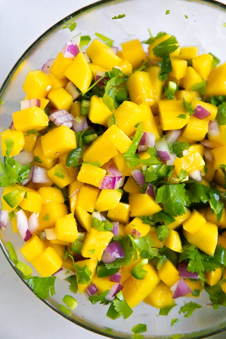 Glass mixing bowl filled with mixed together mango salsa.