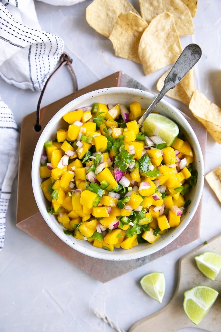 Mango salsa with tortilla chips and garnished with fresh lime wedges.