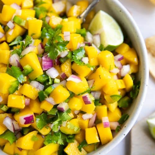 Overhead image of a large white bowl filled with mango salsa made with mango, red onion, cilantro, and lime juice.